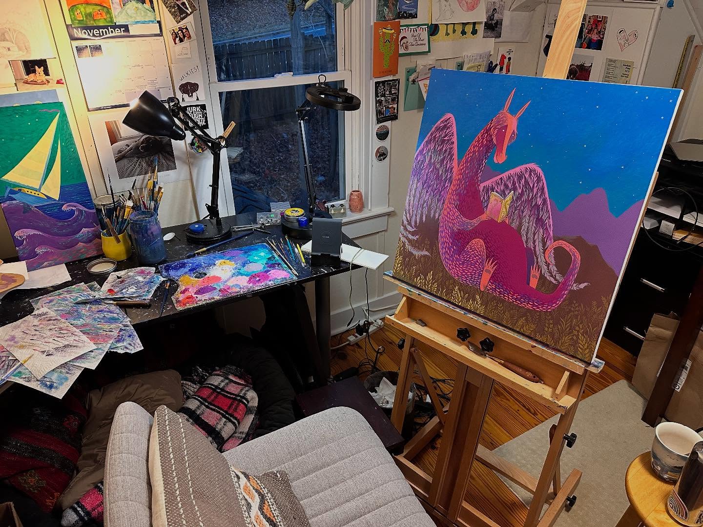 Elaine Thompson's studio workspace with easel, paints, and a vibrant dragon painting in progress